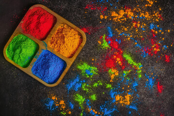 Organic multicolored bright colors of Holi in different colors in a wooden plate on a dark background for the celebration of the Holi festival, view from above
