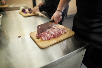 chef cuts chicken meat with a kitchen axe. hands cut chicken meat into pieces. The butcher cuts a chicken carcass with a kitchen ax on a cutting board for cooking.