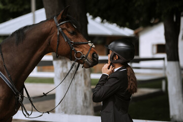 Attractive female equestrian in riding helmet looking at horse in horse club.