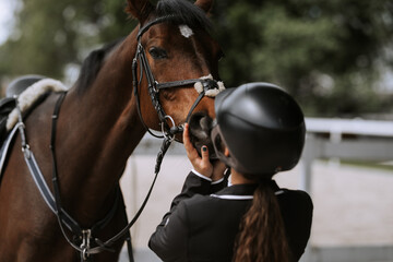 Obraz premium Attractive female equestrian in riding helmet looking at horse in horse club.