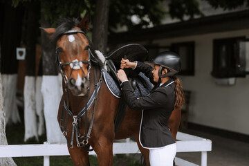 Girl rider adjusts saddle on her horse to take part in horse races.