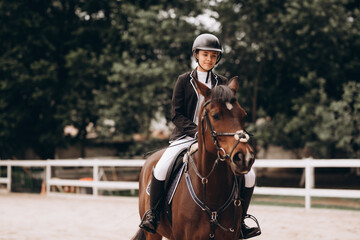 Young woman in special uniform and helmet riding horse. Equestrian sport - dressage.