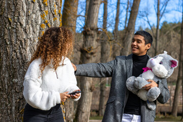 Boyfriend giving a teddy to girlfriend outdoors. Young latin man giving teddy bear to girlfriend