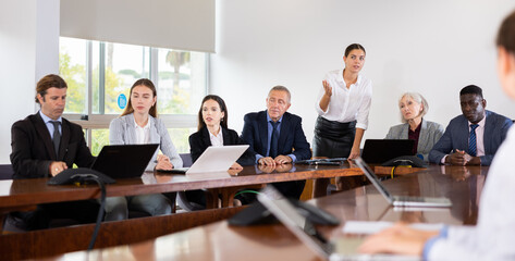 Young elegant businesswoman making presentation to colleagues in modern meeting room