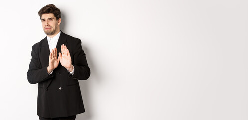 Image of stylish handsome man in black suit, cringe from something embarrassing, declining offer...