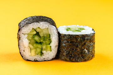 Japanese mini sushi rolls with cucumber, rice and nori on yellow background.