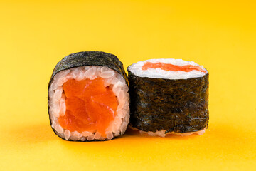 Mini sushi rolls with salmon, rice and nori on yellow background.