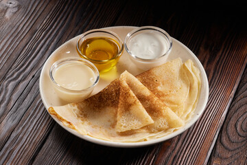 Pancakes with honey condensed milk and sour cream on white plate on wooden table