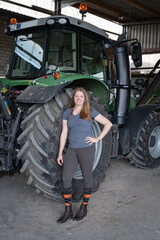 Junge Frau steht neben einen farbereiten Traktor, in einer Maschinenhalle.