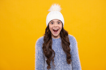 Beautiful winter kids portrait. Teenager girl posing with winter sweater and knit hat on yellow background. Excited face, cheerful emotions of teenager girl.