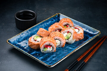 Set of Japanese sushi rolls with seared salmon, cream cheese, avocado, rice, nori, red flying fish caviar and soy sauce.