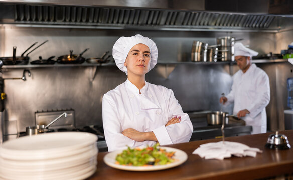 Portrait of female chef with crossed arms along with team of cooks in kitchen of a restaurant