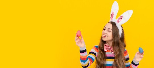 cheerful child in bunny ears and bow tie hold easter eggs on yellow background. Easter child horizontal poster. Web banner header of bunny kid, copy space.