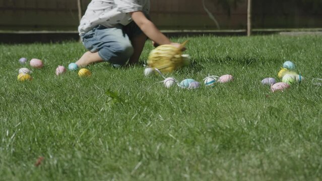 easter egg hunt traditional spring game falling down colorful easter eggs on green grass and little kid boy running on green grass pick up collecting easter eggs into basket. child sit on lawn have