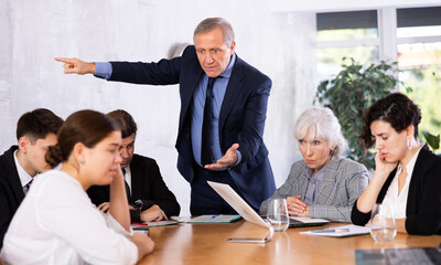 Irritated aged chief scolding subordinates, pointing out shortcomings and omissions in work during office meeting