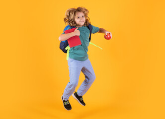 Fototapeta na wymiar Kid jump and enjoy school. Photo of excited little school jumping holding book, empty space isolated yellow background. Amazed school child jump with backpack.