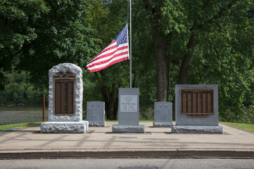 War memorials, inscribed headstones and American flag honoring US war veterans in a graveyard.