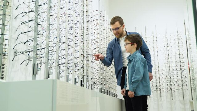 Family buy glasses. Father and son in a blue shirts choosing glasses