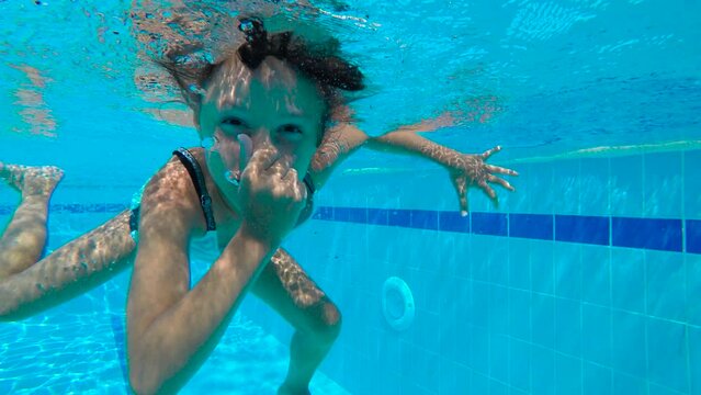 Happy child dives into the pool. A happy little girl close her nose and jump under pool water in the sun rays. A concept of joyful children vacation in summer.