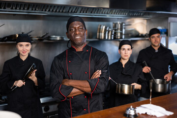 Team of focused chefs with African man head chef posing together in restaurant kitchen