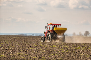 A farmer in an agricultural tractor at a farm fertilizing an arable field, a crucial step in crop...