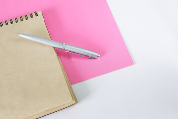 A silver fountain pen and an eco-friendly notepad made from recycled materials lie on a pink and white surface. Copy space.