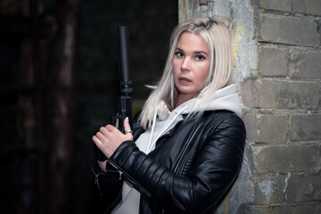 Obraz na płótnie Canvas A beautiful girl with ashy hair color with a pistol with a silencer in a destroyed building in the war.