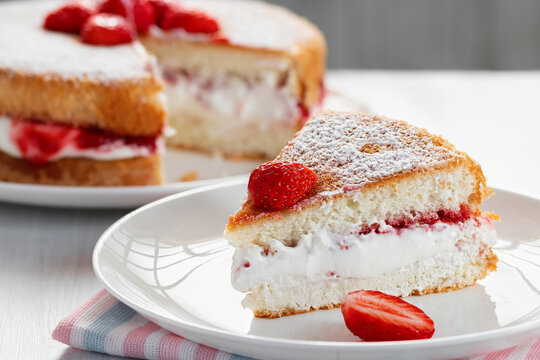 Piece of Victoria biscuit cake with whipped cream, jam and fresh strawberries