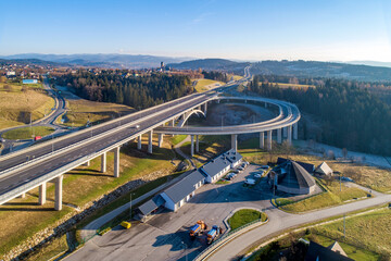 New highway in Poland on national road no 7, E77, called Zakopianka.  Overpass junction with a traffic circle, viaducts, slip roads and cars. Skomielna Biala village in the background. Aerial view