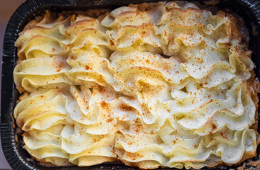 Mashed potatoes, boiled puree in cast iron pot on dark rustic background with freshly-cracked red...