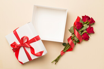 Open gift box with red roses on color background, top view