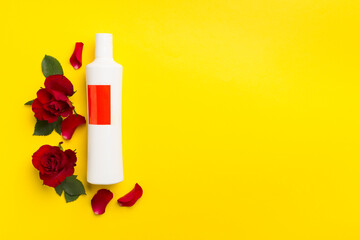 Cosmetic bottle and red roses on color background, top view