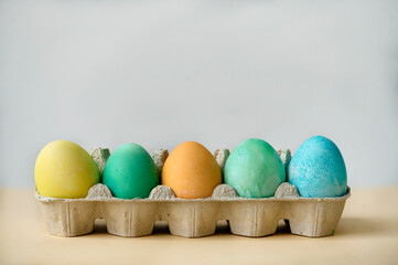 colorful painted Easter eggs in a paper egg container on a beige background. Side view