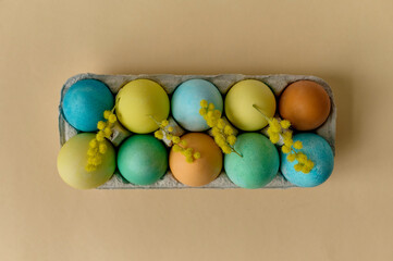 colorful painted Easter eggs in a paper egg container on a beige background. Top view