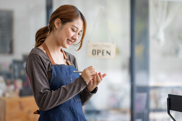 Shot of smiling young cafe show owner Asian woman standing with arms crossed and Open sign on the glass door. Portrait of asian tan woman barista cafe SME entrepreneur seller business concept.