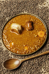 Traditional recipe for stewed lentils with chorizo and vegetables in a gold-rimmed plate on dried lenjetas and a wooden spoon