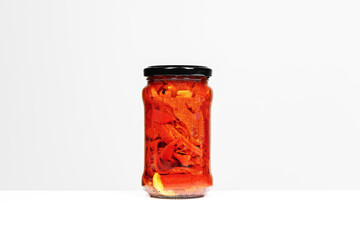 Image of a can of roasted pepper strips with a clove of garlic in the background inside a glass jar