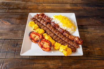 A plate with skewers cooked in the Middle Eastern style of different kinds of meat accompanied by roasted tomatoes and rice with sauce