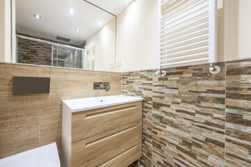 Bathroom with white porcelain sink above chest of drawers with wooden drawers and frameless mirror...