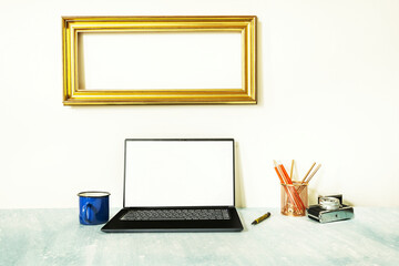 Fototapeta premium Image of a laptop on a blue surface next to a vintage camera, a coffee mug and a gold frame on the wall