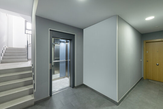 Interior elevator of a modern apartment building clad in mirror panels next to a set of stairs with gray treads
