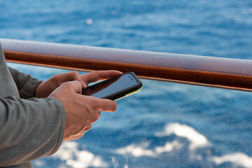 Hand of man using mobile smart cell phone on a ship with the blue ocean background and copy space with a shallow depth of field