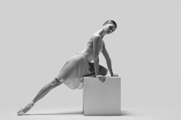 Young ballerina practicing dance moves on cube, toned in black and white