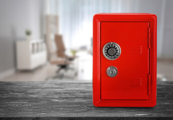 Red closed steel safe with mechanical lock on grey wooden table indoors. Space for text