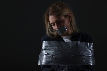 Woman taped up and taken hostage on dark background. Space for text