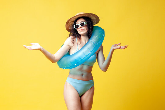 young insecure brunette girl in a blue swimsuit with a swimming inflatable ring spreads her arms