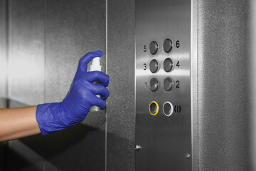 Woman cleaning buttons panel in elevator with detergent spray, closeup