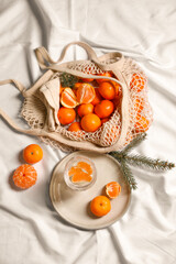 Delicious ripe tangerines, glass with sparkling wine and fir branch on white bedsheet, flat lay