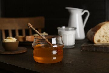 Jar with honey, milk, bread and butter on wooden table