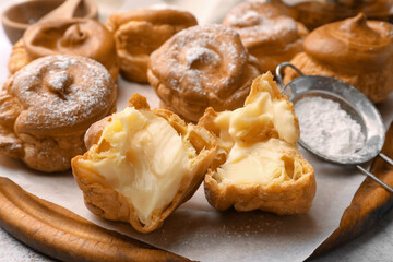 Delicious profiteroles filled with cream on wooden board, closeup